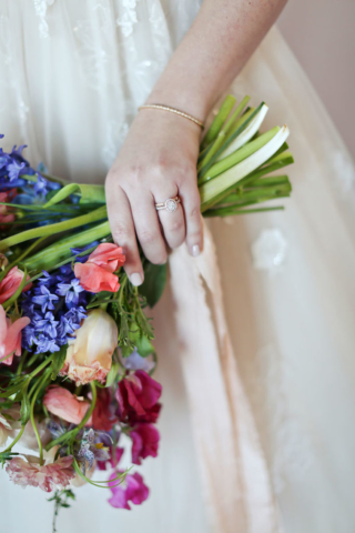 closeup of wedding ring on hand holding bright wedding flower bouquet