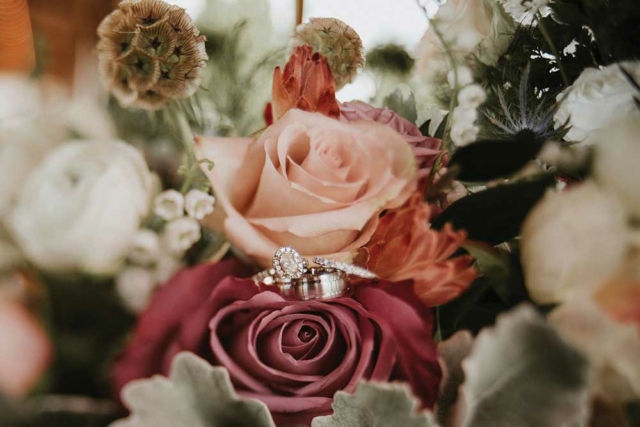 closeup wedding bands sitting on dusty rose flower bouquet