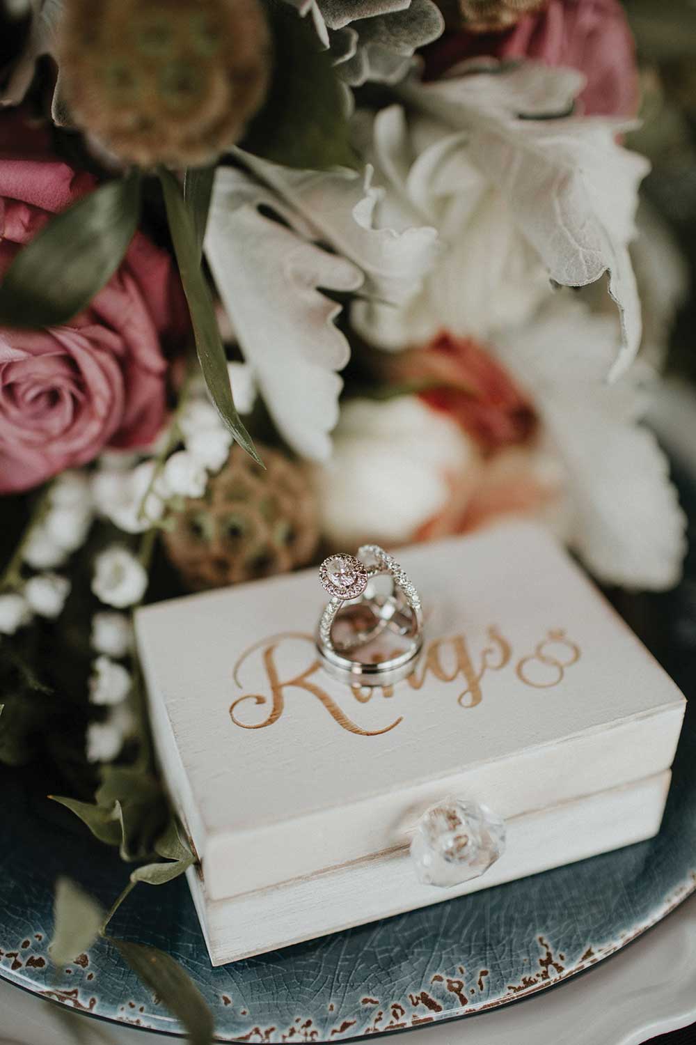 wedding rings closeup under bouquet on top of Rings box