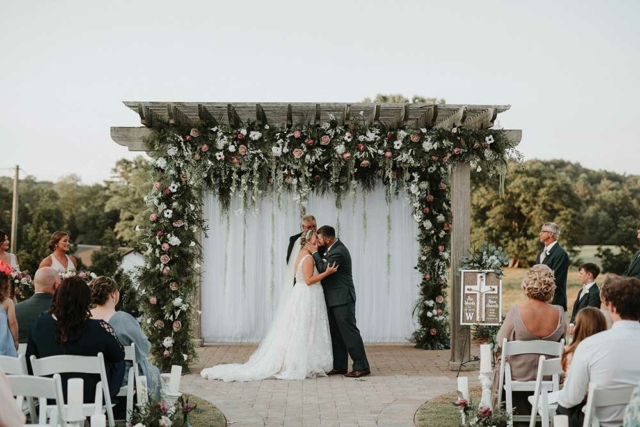 wedding ceremony, couple kissing in front of pastor and flowery arbor