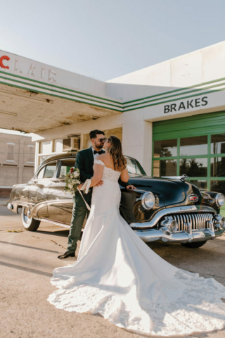 married couple emerald and gold standing in front of vintage car and garage