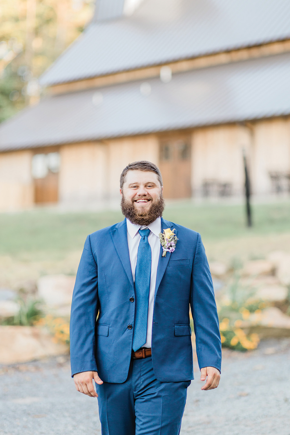 groom in navy blue suit smiling outside barn location